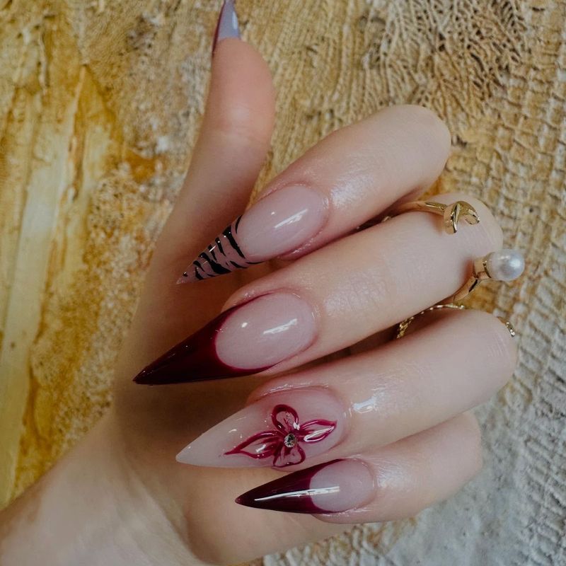 Nude stiletto nails with burgundy French tips and flower art by Nini Nail Bar